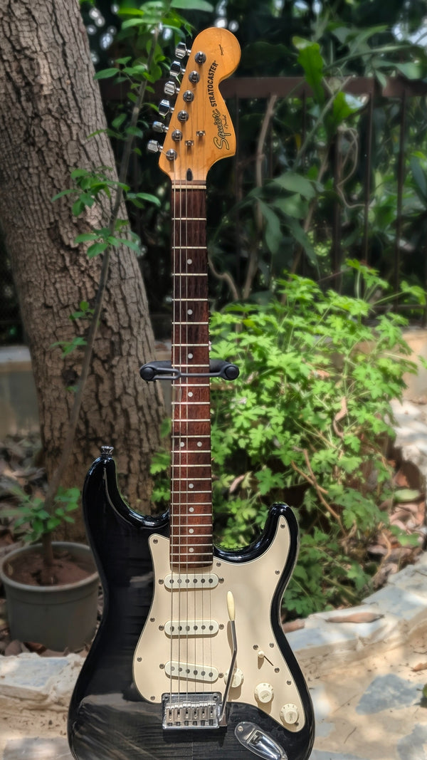 Black electric guitar with a wooden neck against a natural background